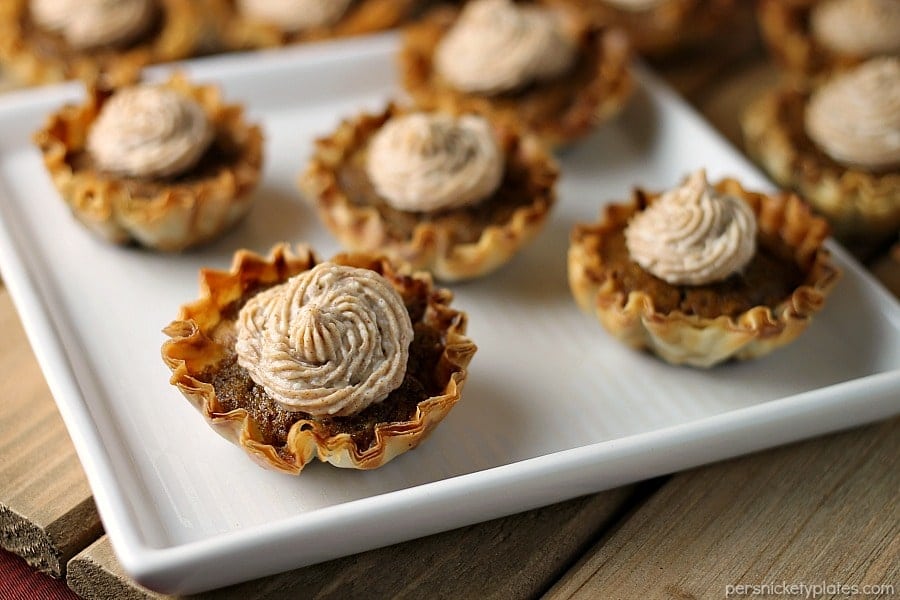 Mini Sweet Potato Pies with Cinnamon Cream Cheese Frosting are super easy to make but look fancy. Impress your guests with these bite sized treats! | www.persnicketyplates.com #pie #sweetpotatopie #thanksgiving #minidessert #dessert close up of 5 mini sweet potato pies on white square plate