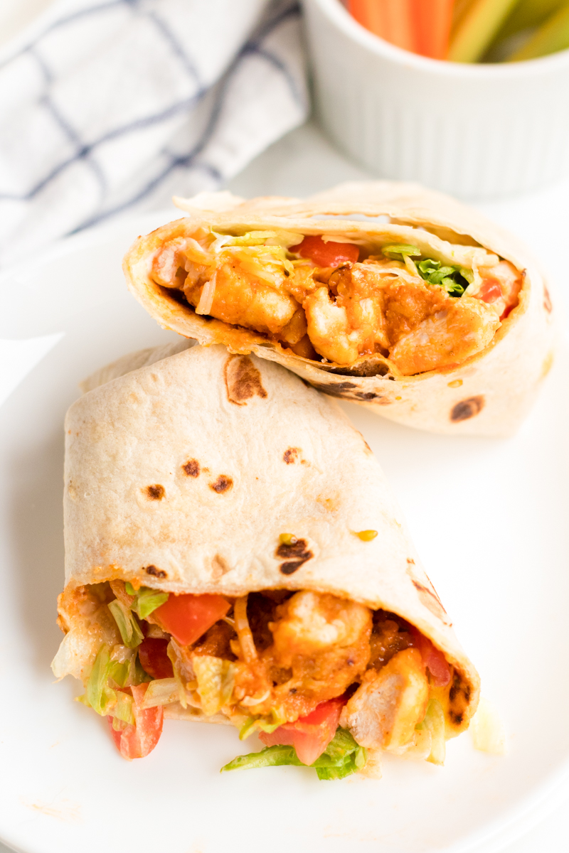 If you like the Buffalo Ranch Chicken Wrap from Buffalo Wild Wings, you'll love this lightened up homemade version! Lightly breaded buffalo chicken pieces wrapped up in a soft tortilla with ranch dressing, shredded lettuce, cheese, and tomatoes make a great dinner or the perfect game day meal! | www.persnicketyplates.com sliced buffalo ranch chicken wrap on a white plate