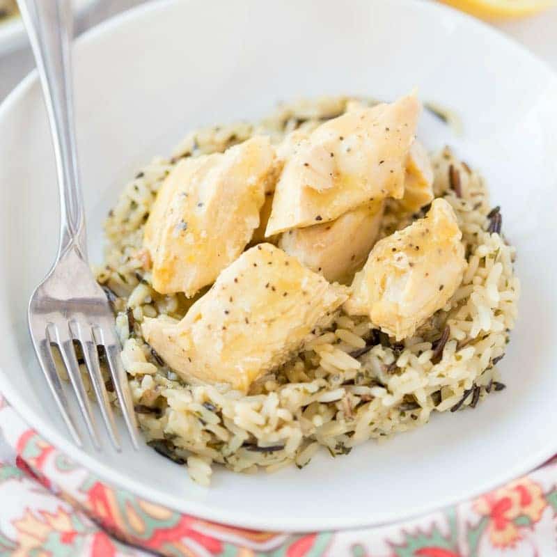 This Crock Pot Lemon Chicken is so easy and perfect for a busy weeknight. This 4 ingredient, quick chicken dinner is amazingly flavorful and sure to be your new favorite meal. Serve with vegetables and ready to serve rice for a fast healthy dinner! | www.persnicketyplates.com lemon chicken on a bed of rice in a white bowl with a fork