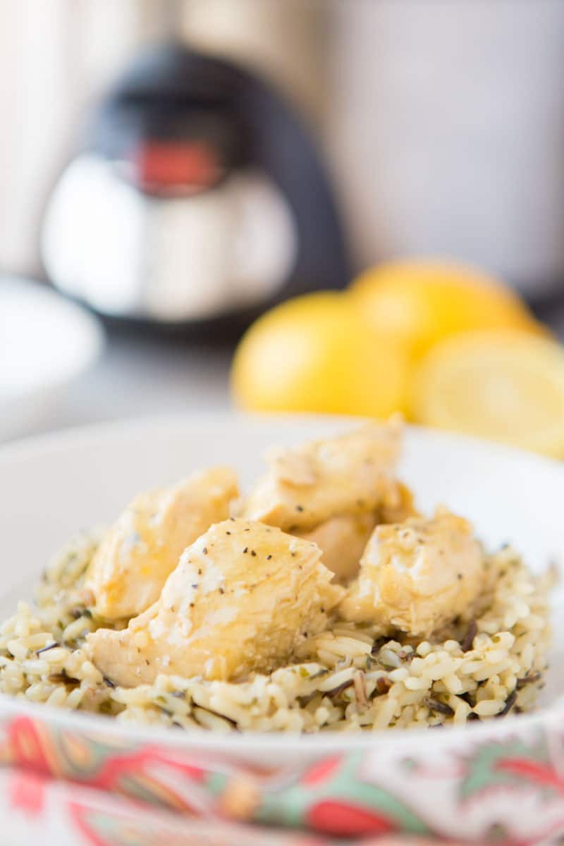 This Crock Pot Lemon Chicken is so easy and perfect for a busy weeknight. This 4 ingredient, quick chicken dinner is amazingly flavorful and sure to be your new favorite meal. Serve with vegetables and ready to serve rice for a fast healthy dinner! | www.persnicketyplates.com lemon chicken on a bed of rice with slow cooker & lemons in background