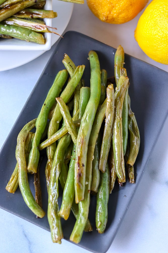 Oven roasted garlic green beans are a super simple and healthy side dish that I can never stop eating! Only five ingredients in this side dish that pairs well with just about anything. | www.persnicketyplates.com garlic green beans on grey platter with lemons in background