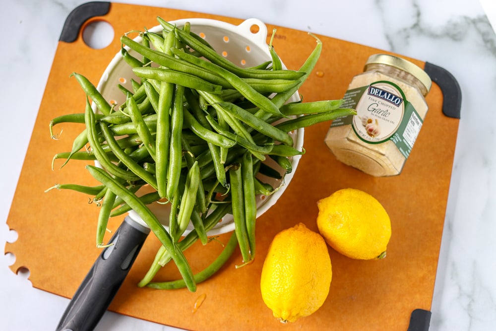 Oven roasted garlic green beans are a super simple and healthy side dish that I can never stop eating! Only five ingredients in this side dish that pairs well with just about anything. | www.persnicketyplates.com fresh green beans in colander with lemons and garlic