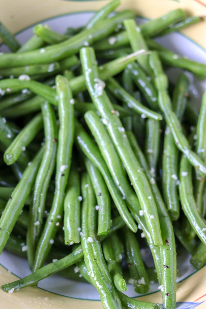 Oven roasted garlic green beans are a super simple and healthy side dish that I can never stop eating! Only five ingredients in this side dish that pairs well with just about anything. | www.persnicketyplates.com garlic green beans prepped in a bowl with garlic