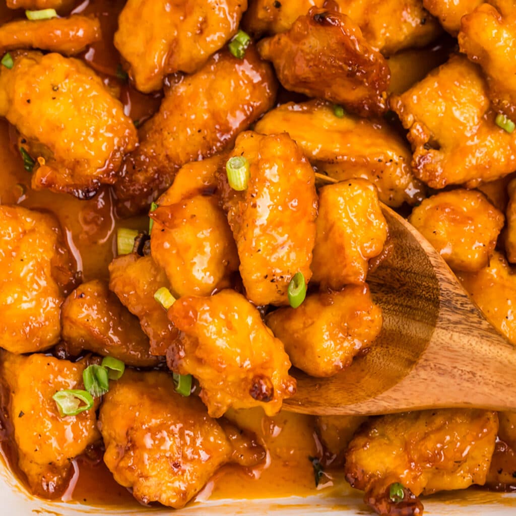 wooden spoon lifting a scoop of sweet & sour chicken.