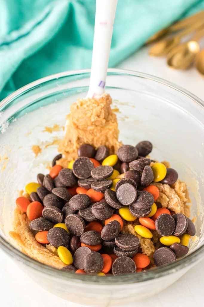 mixing bowl of cookie dough topped with chocolate chips & reese's pieces.