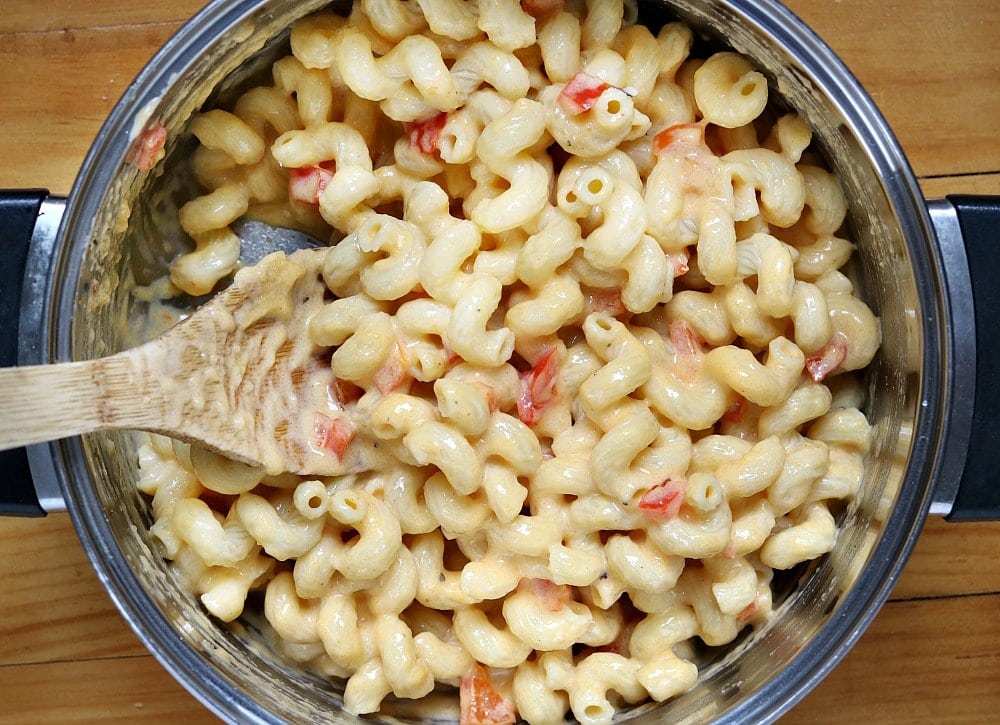 Hard Rock Cafe Twisted Macaroni & Cheese is cavatappi pasta tossed in a slightly spicy cheese sauce with roasted red peppers and topped with Parmesan parsley breadcrumbs. A copycat version of a favorite restaurant dish! | www.persnicketyplates.com cheesy pasta in a saucepan with wooden spoon