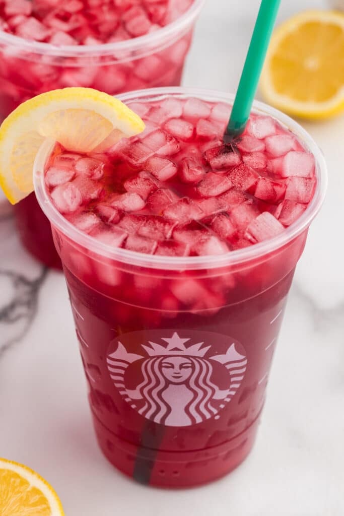 A Starbucks plastic cup with iced passion tea lemonade, green straw, and lemon slice.