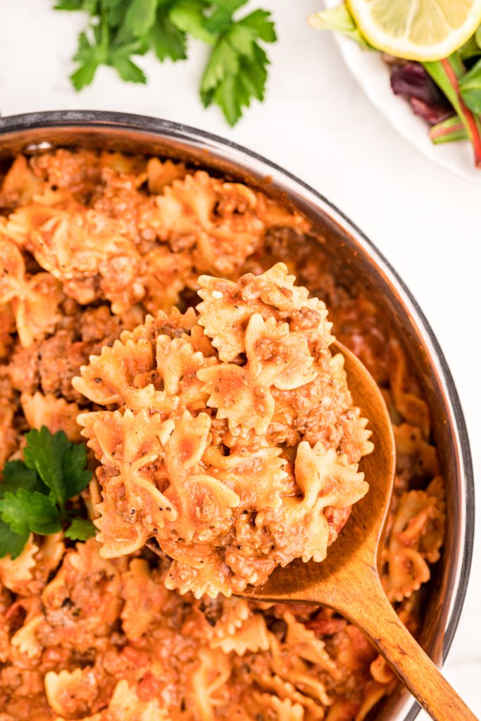 wooden spoon scooping bow tie pasta from a skillet.