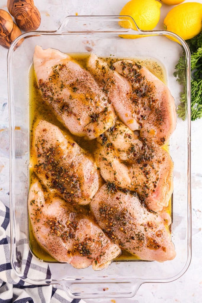 overhead shot of raw chicken breasts coated in garlic butter in a bakin dish.