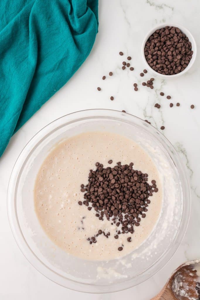 overhead shot of mini chocolate chips poured into muffin batter.