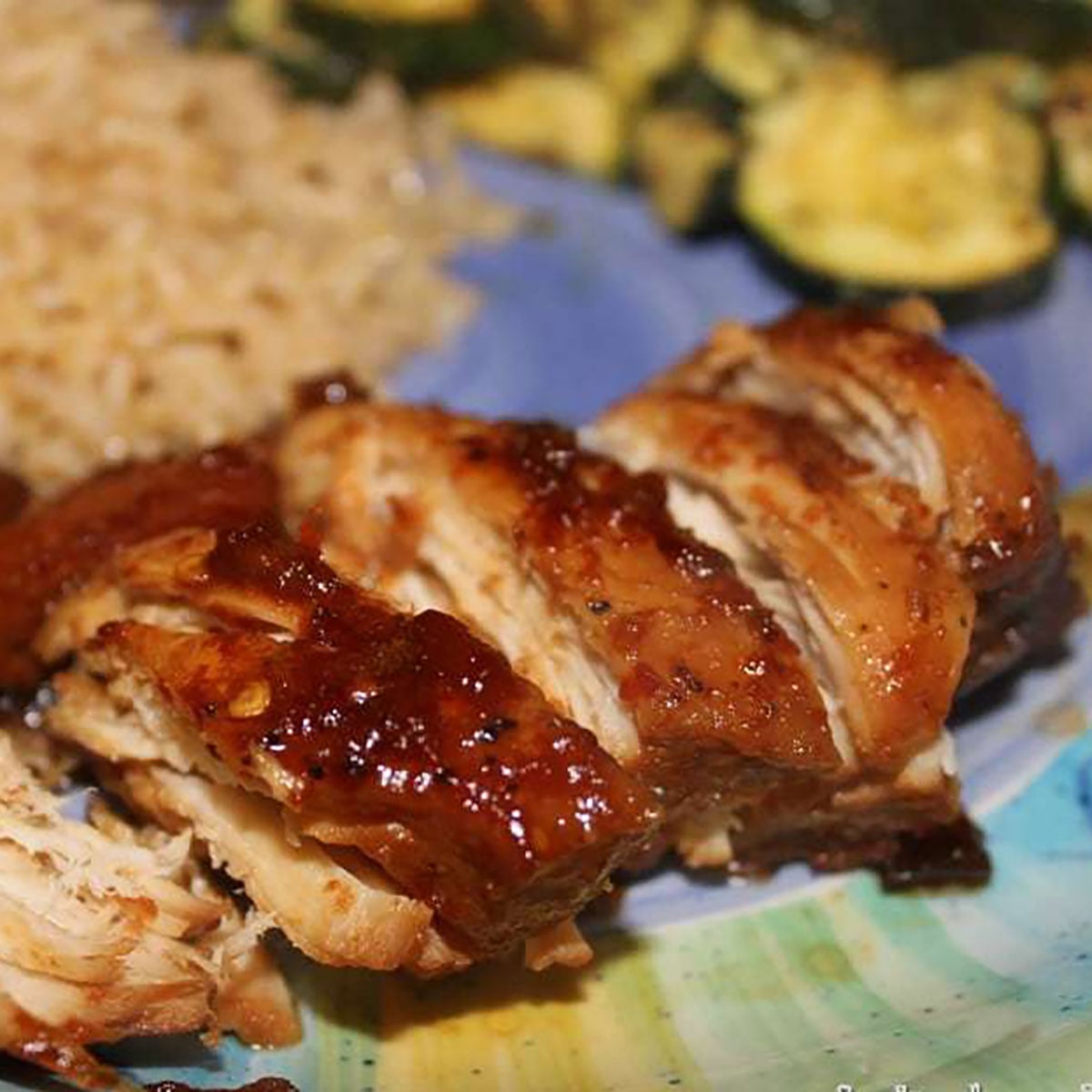 sliced honey bourbon chicken on a plate with rice and zucchini.