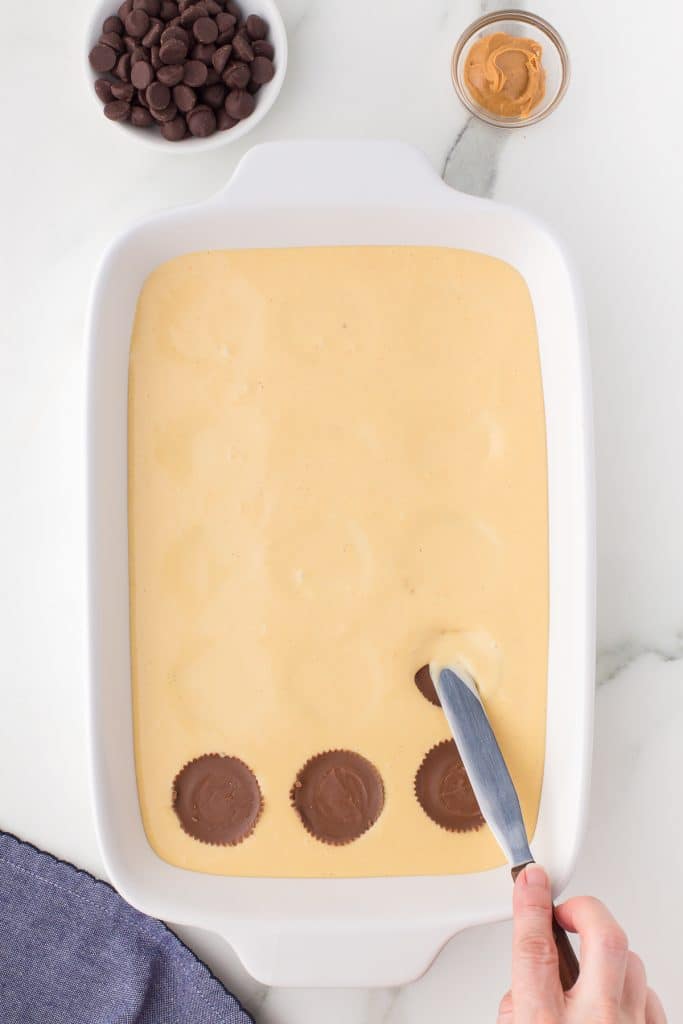 spreading cheesecake batter over peanut butter cups in a 9x13 pan.