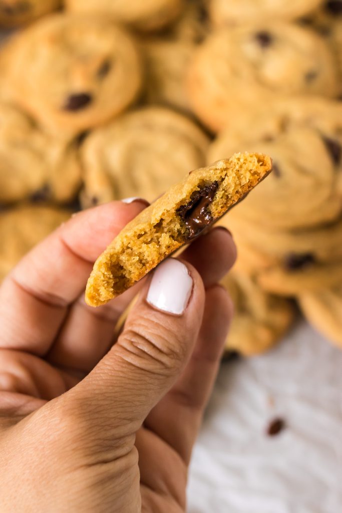 hand holding a chocolate chip cookie with a bite missing.