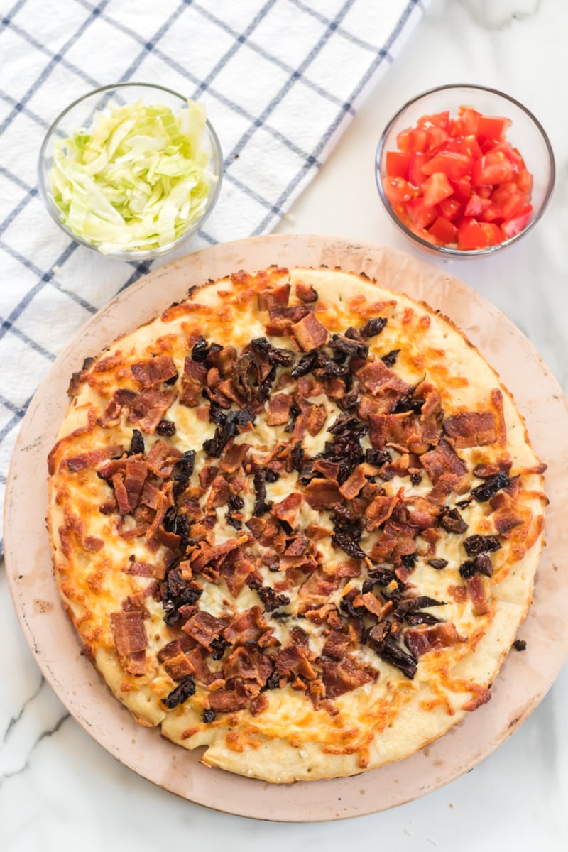 This BLT Pizza is semi-homemade and topped with cheese, bacon, lettuce, and tomatoes then drizzled with ranch dressing - a super easy meal for pizza night at home! | www.persnicketyplates.com pizza with melted cheese ready to top with lettuce & tomatoes for blt pizza