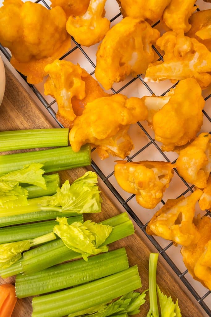 buffalo cauliflower on a wire rack next to celery sticks.