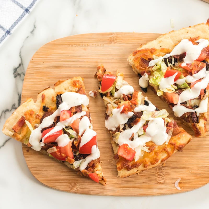 This BLT Pizza is semi-homemade and topped with cheese, bacon, lettuce, and tomatoes then drizzled with ranch dressing - a super easy meal for pizza night at home! | www.persnicketyplates.com three slices of blt pizza on a wood cutting board