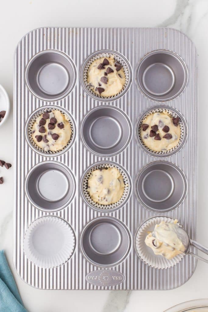 overhead shot of muffin batter being scooped into a muffin pan.