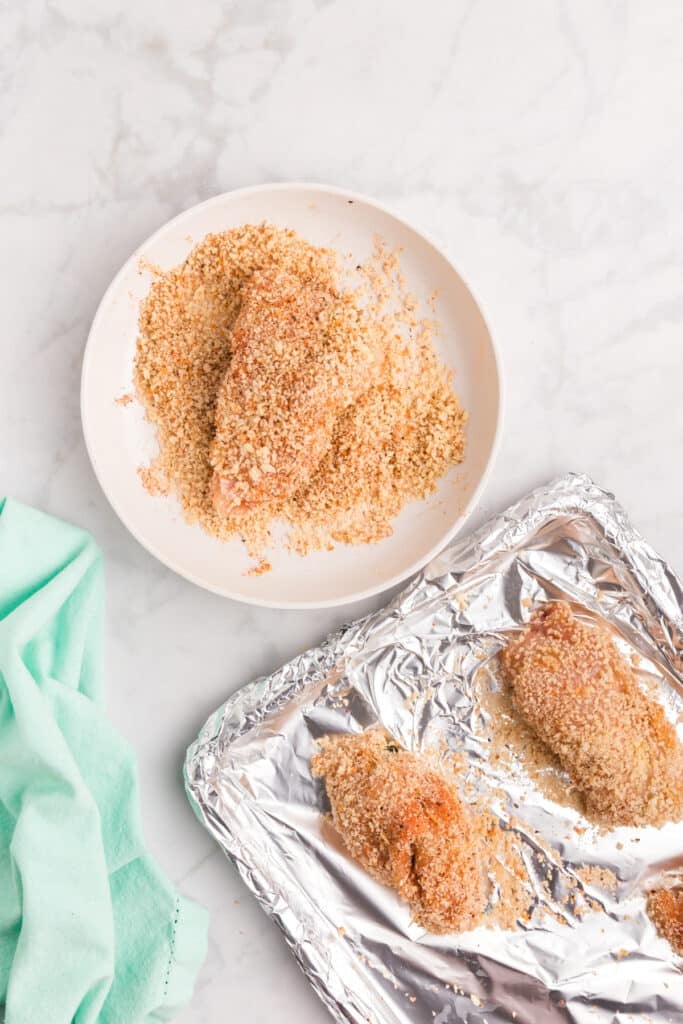 Chicken breast coated in seasoned breadcrumbs in a bowl, ready for baking.