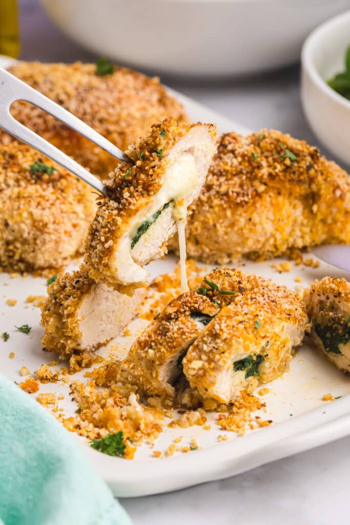 A fork lifting a piece of Cajun stuffed chicken with melted cheese stretching.