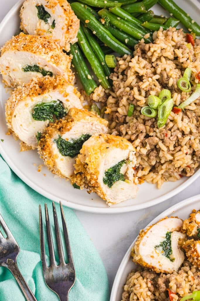 sliced stuffed chicken breast on a plate with dirty rice and green beans.