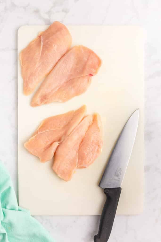 a knife laying next to two butterflied chicken breasts.