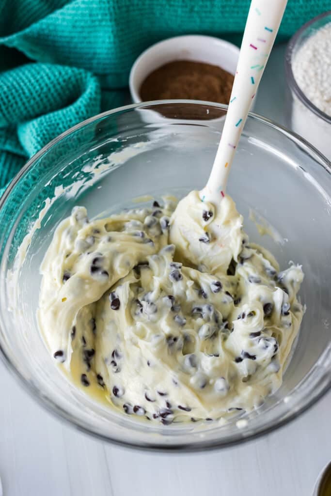 A bowl of creamy cheesecake filling with mini chocolate chips, stirred with a spatula.