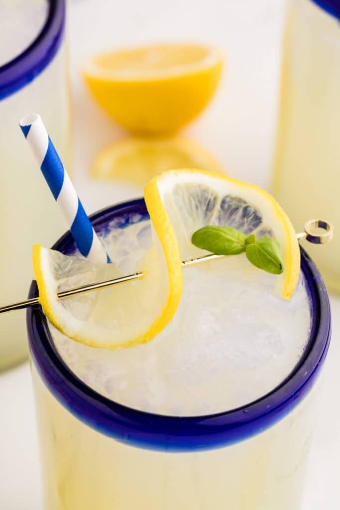A glass of boozy frozen lemonade garnished with a lemon slice and fresh basil.