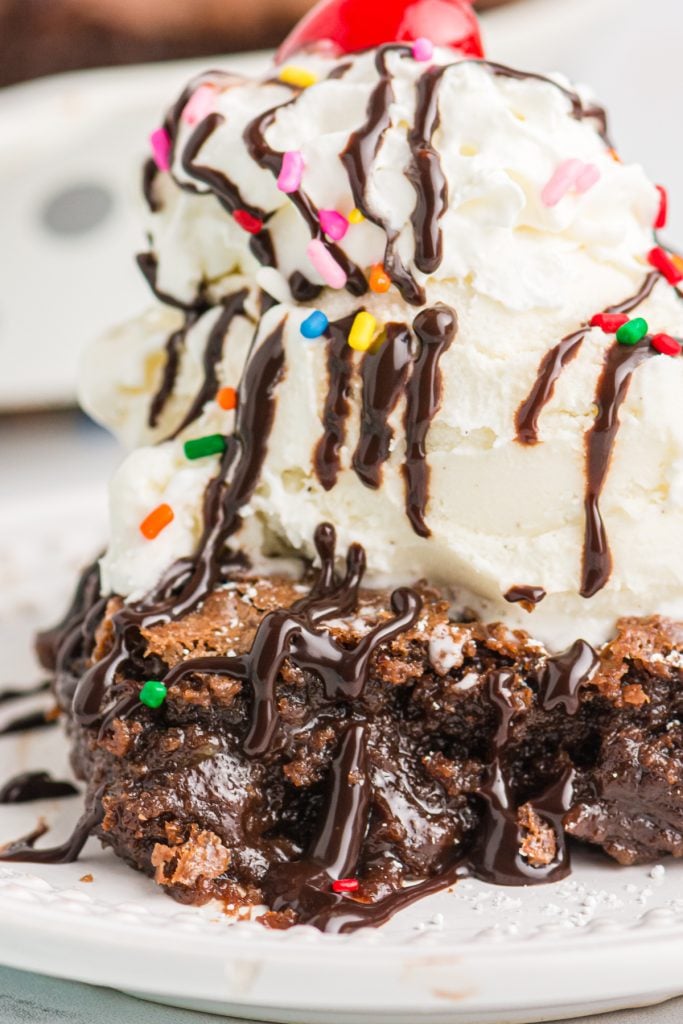 hot fudge pie topped with ice cream, fudge, and rainbow sprinkles.
