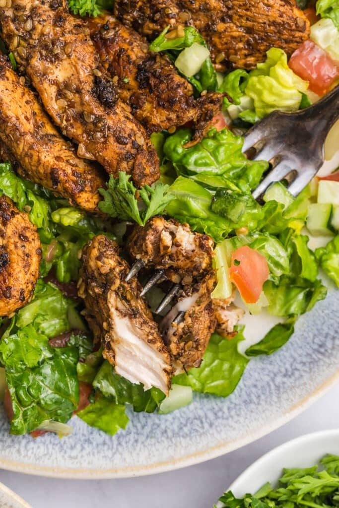 bite of chicken on a fork in a salad.