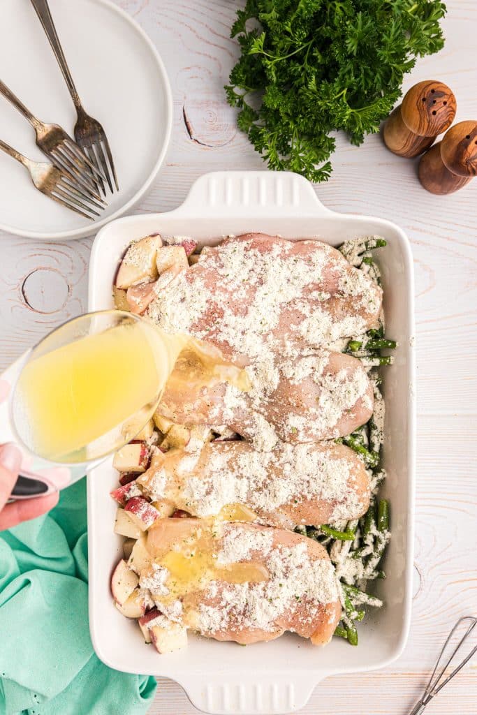 butter being poured onto raw chicken in a baking dish.