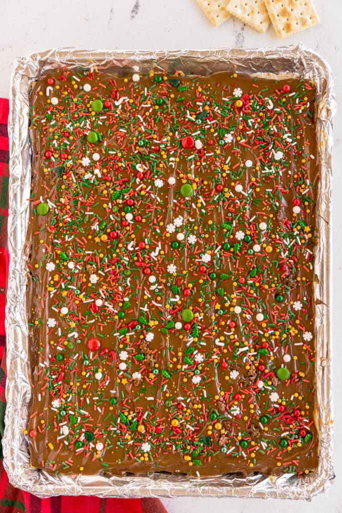 A baking tray of chocolate-covered Christmas crack decorated with colorful holiday sprinkles.