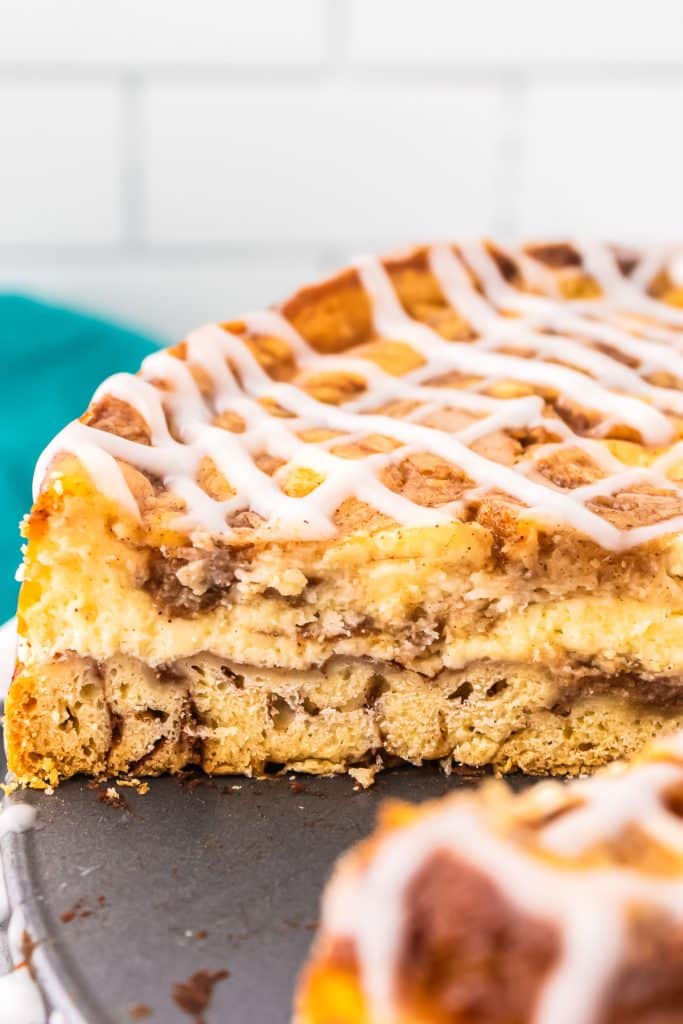 side view of a cinnamon roll cheesecake with a slice missing.
