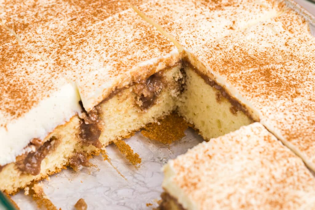 side view of a sliced cinnamon roll poke cake with cream cheese frosting.