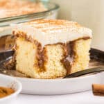 slice of cinnamon roll poke cake with cream cheese frosting on a plate.