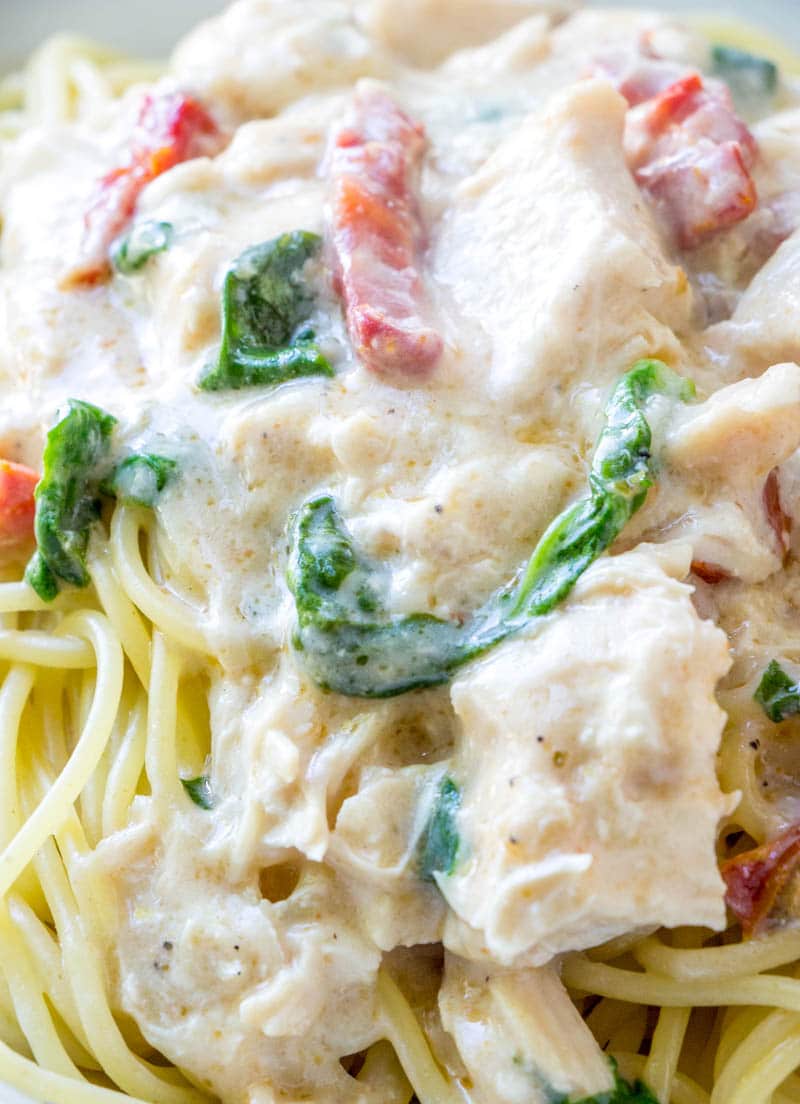 Five ingredient, super simple, Crock Pot Chicken Alfredo takes no time at all to throw together in the slow cooker. This easy crockpot chicken alfredo recipe will become a staple in your meal plan. close up of chicken alfredo pasta with spinach & sun dried tomatoes