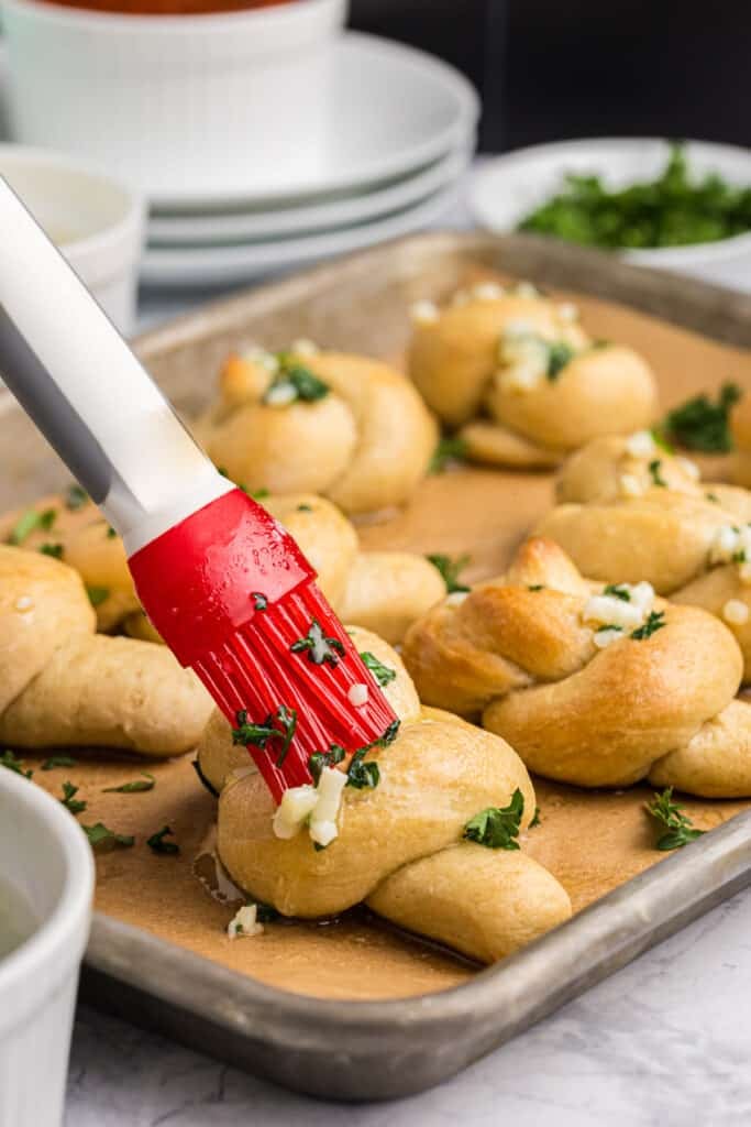 pastry brush brushing garlic butter onto dough knots.