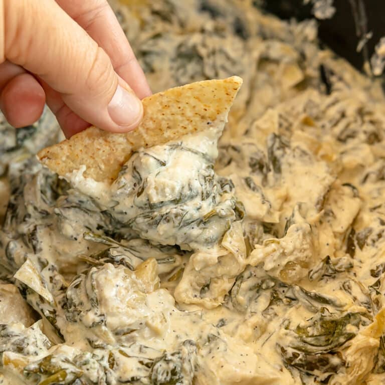 hand dipping a tortilla chip into crockpot spinach artichoke dip.