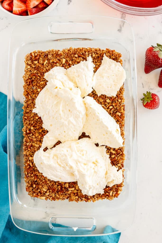 cream cheese layer being spread onto a pretzel crust.