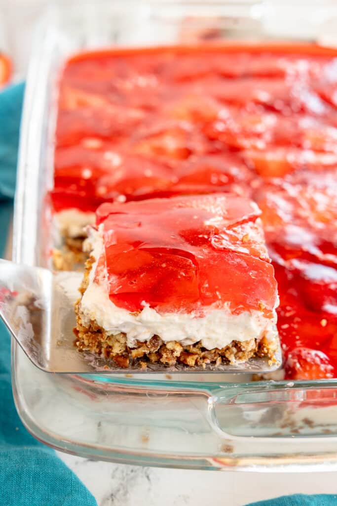lifting a slice of strawberry pretzel dessert from the pan.