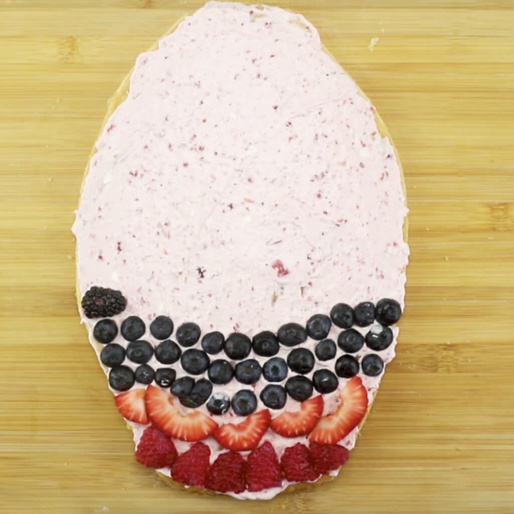 partially decorated easter egg fruit pizza with cream cheese frosting.