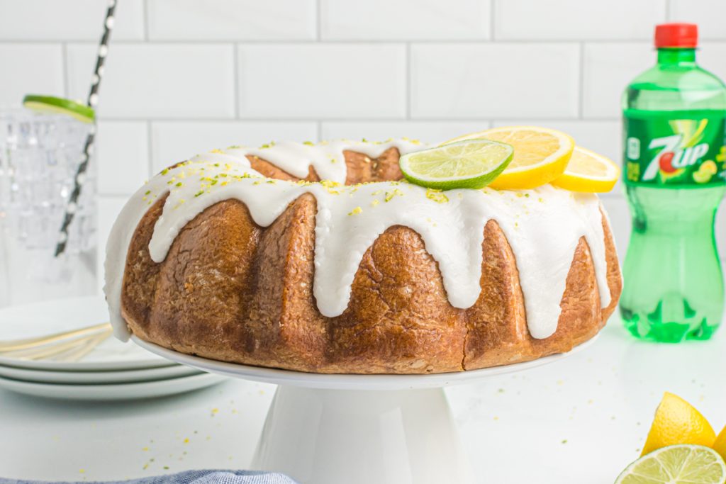 bundt cake covered in glaze on a cake stand with 7up soda in the background.