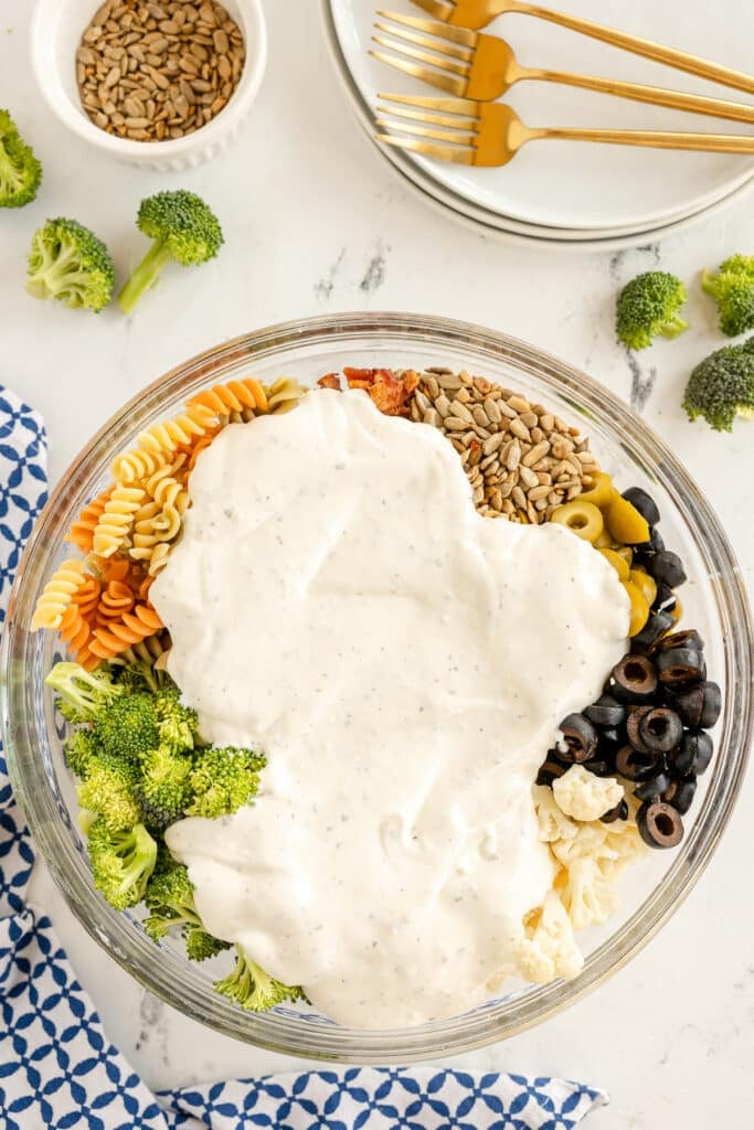 ranch dressing poured over pasta salad ingredients.