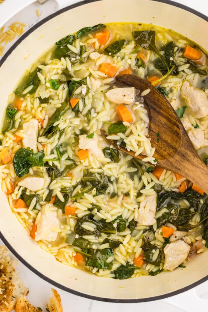 pot of chicken soup with spinach and a wooden spoon.