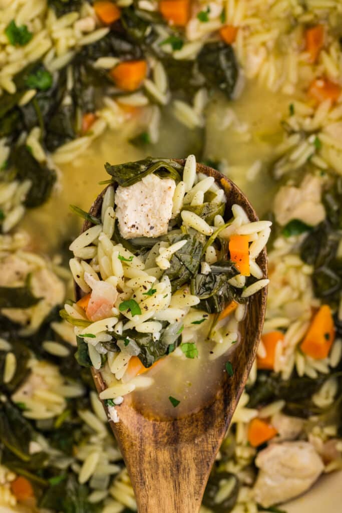 wooden spoon lifting a scoop of lemon chicken orzo soup.