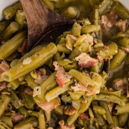 Green beans with bacon and onion on a wooden spoon over a pot.