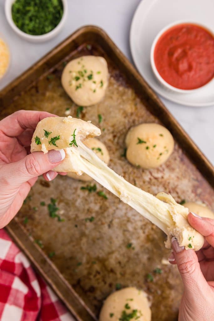 hands pulling a roll with melty cheese stretching between the pieces.