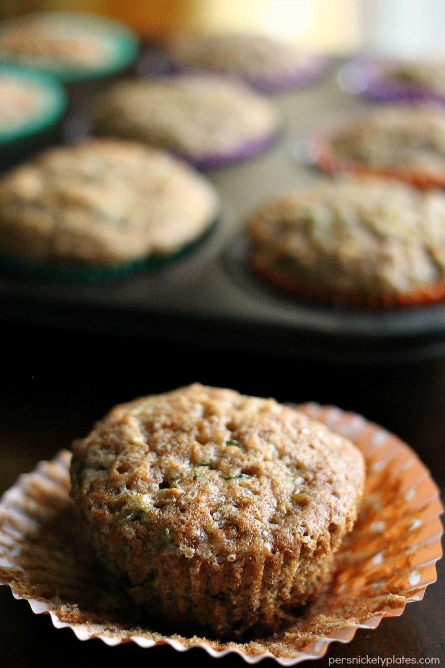 apple and zucchini muffins peels from wrapper with muffin tray in background apple cinnamon zucchini muffin peeled from a cupcake wrapper.