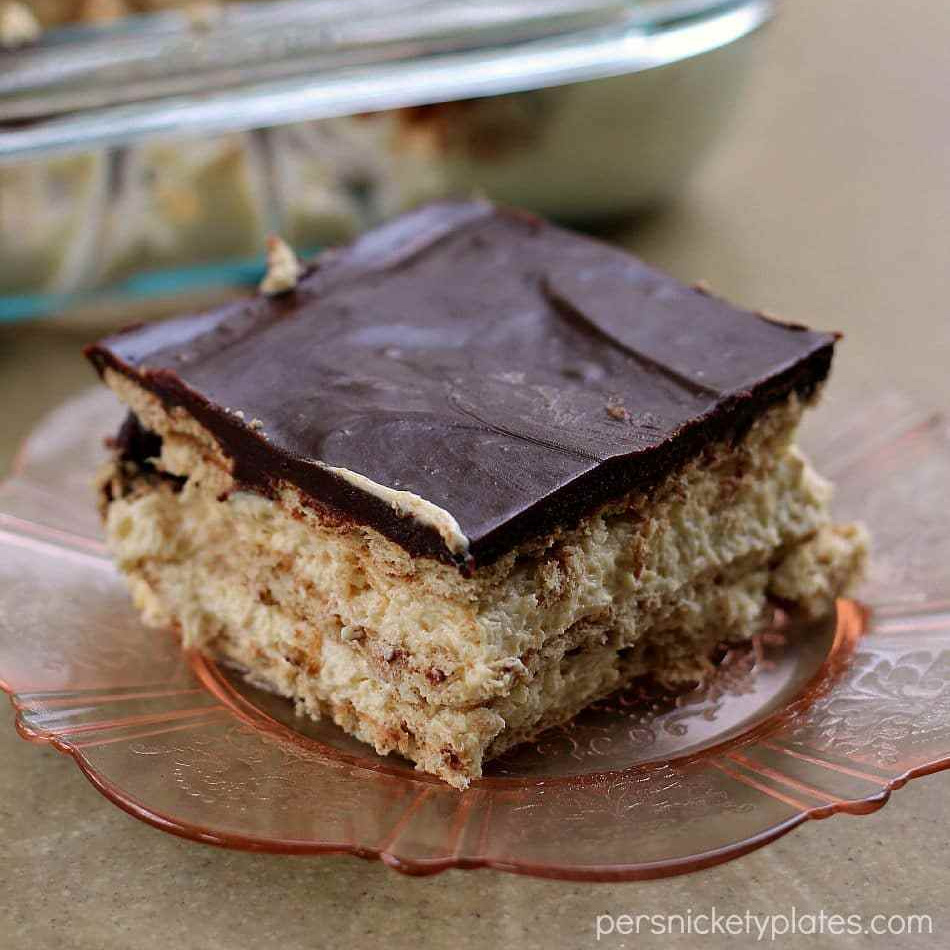 This no bake Chocolate and Peanut Butter Eclair Dessert has layers of graham crackers, layers of peanut butter pudding, a sprinkling of mini chocolate chips, and a chocolate peanut butter frosting. It's a chocolate + peanut butter lovers dream. | www.persnicketyplates.com slice of chocolate peanut butter eclair dessert on pink plate