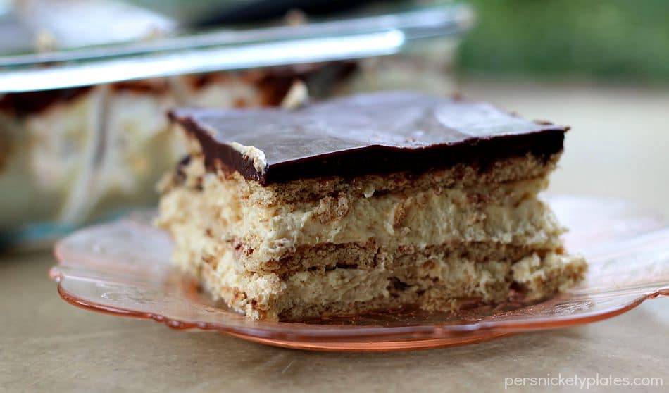 This no bake Chocolate and Peanut Butter Eclair Dessert has layers of graham crackers, layers of peanut butter pudding, a sprinkling of mini chocolate chips, and a chocolate peanut butter frosting. It's a chocolate + peanut butter lovers dream. | www.persnicketyplates.com slice of layered chocolate eclair dessert on pink plate