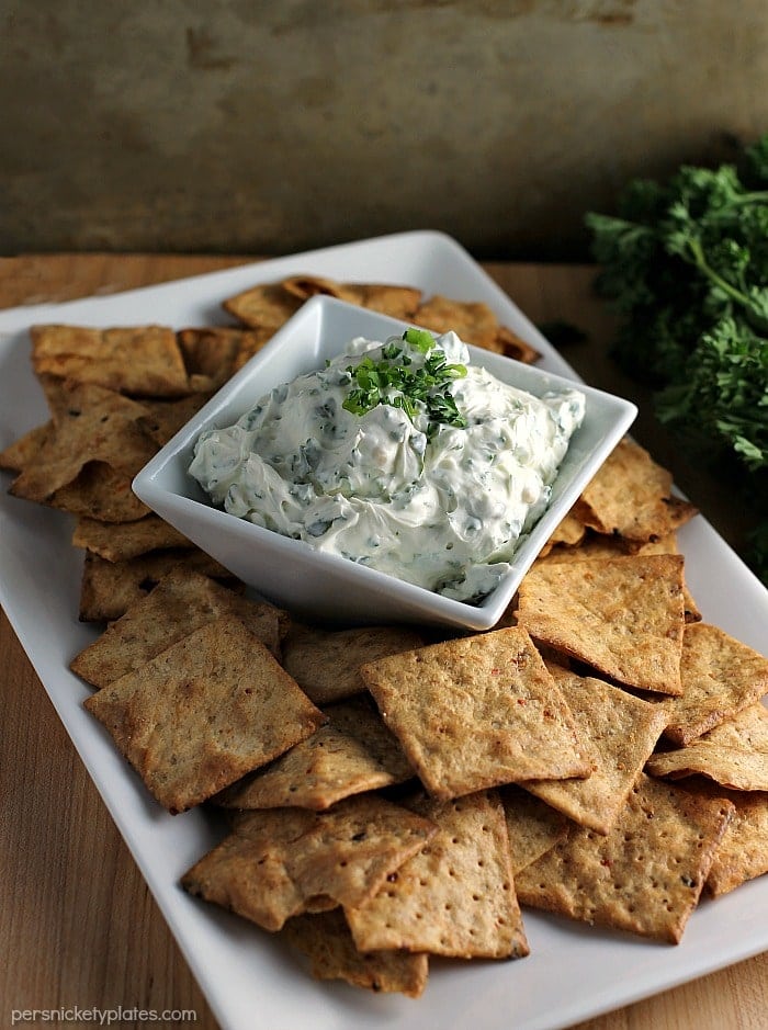 Garlic Herb Dip starts with a cream cheese base then is filled with fresh herbs. Pair this super easy dip recipe with crackers, chips, or veggies to make the perfect quick snack for your next party or game day. | www.persnicketyplates.com #dip #appetizer #easyrecipe #partyfood #garlic garlic herb dip surrounded by chips on white platter